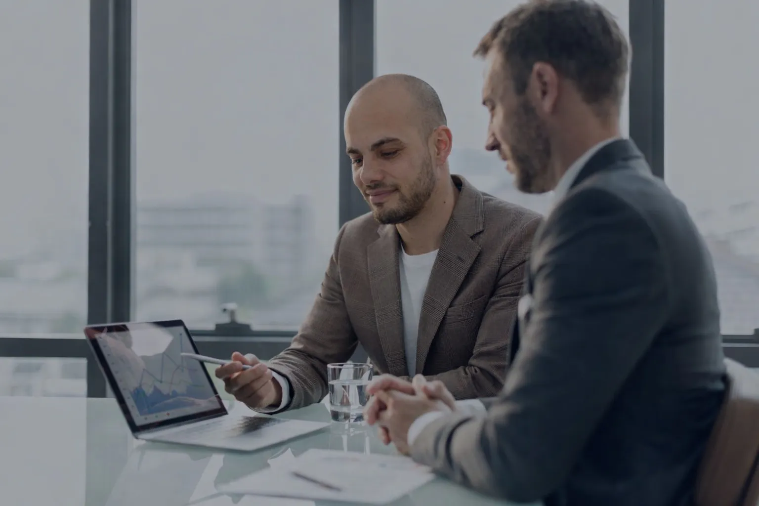 Dois consultores da Mundiempresarial a analisar gráficos de crescimento num portátil num escritório moderno com vista para a cidade, representando soluções de gestão empresarial.