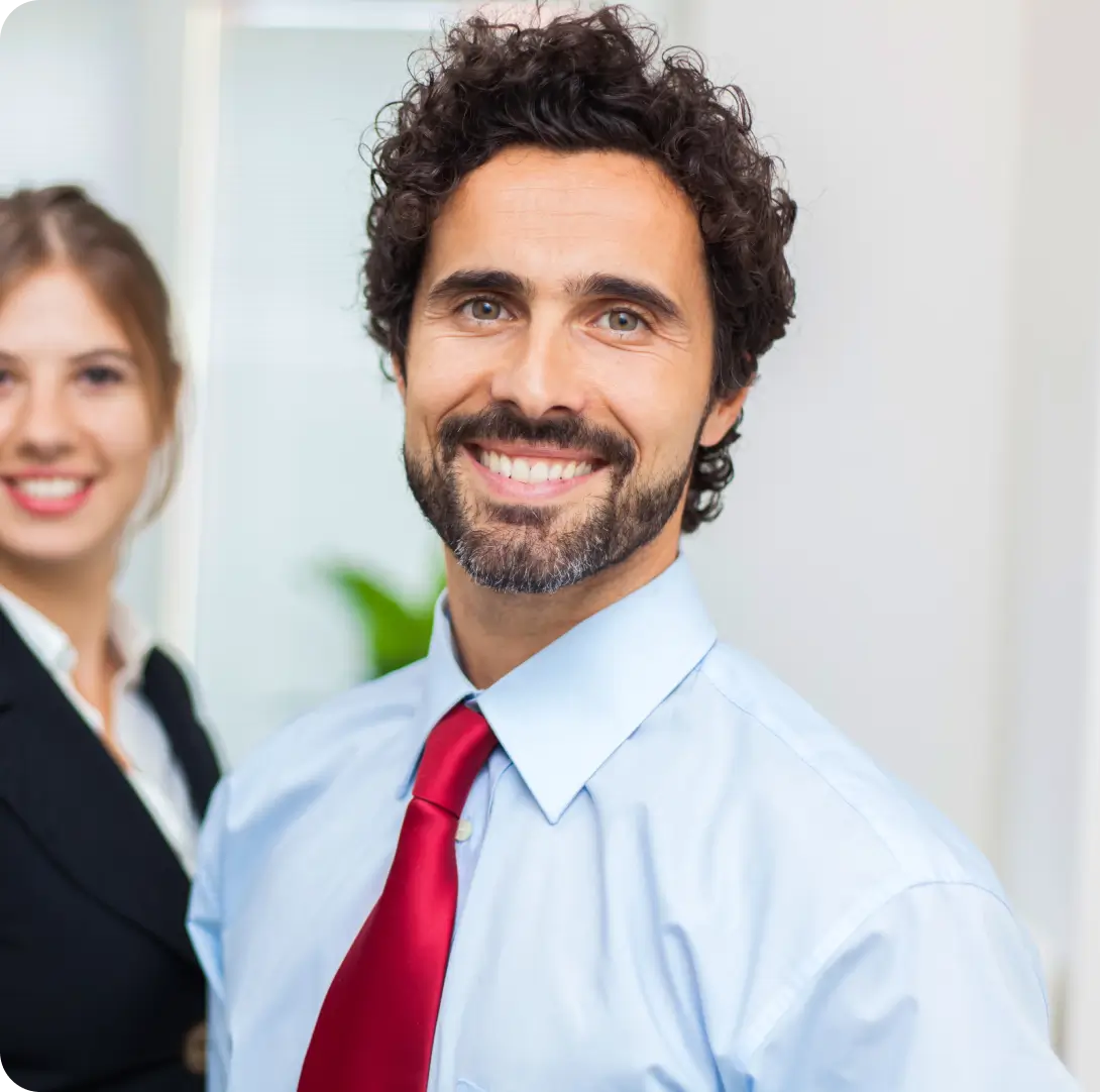 Retrato em primeiro plano de um empresário sorridente e confiante, com uma colega ao fundo, representando a satisfação do cliente com os serviços de contabilidade e consultoria da Mundiempresarial.