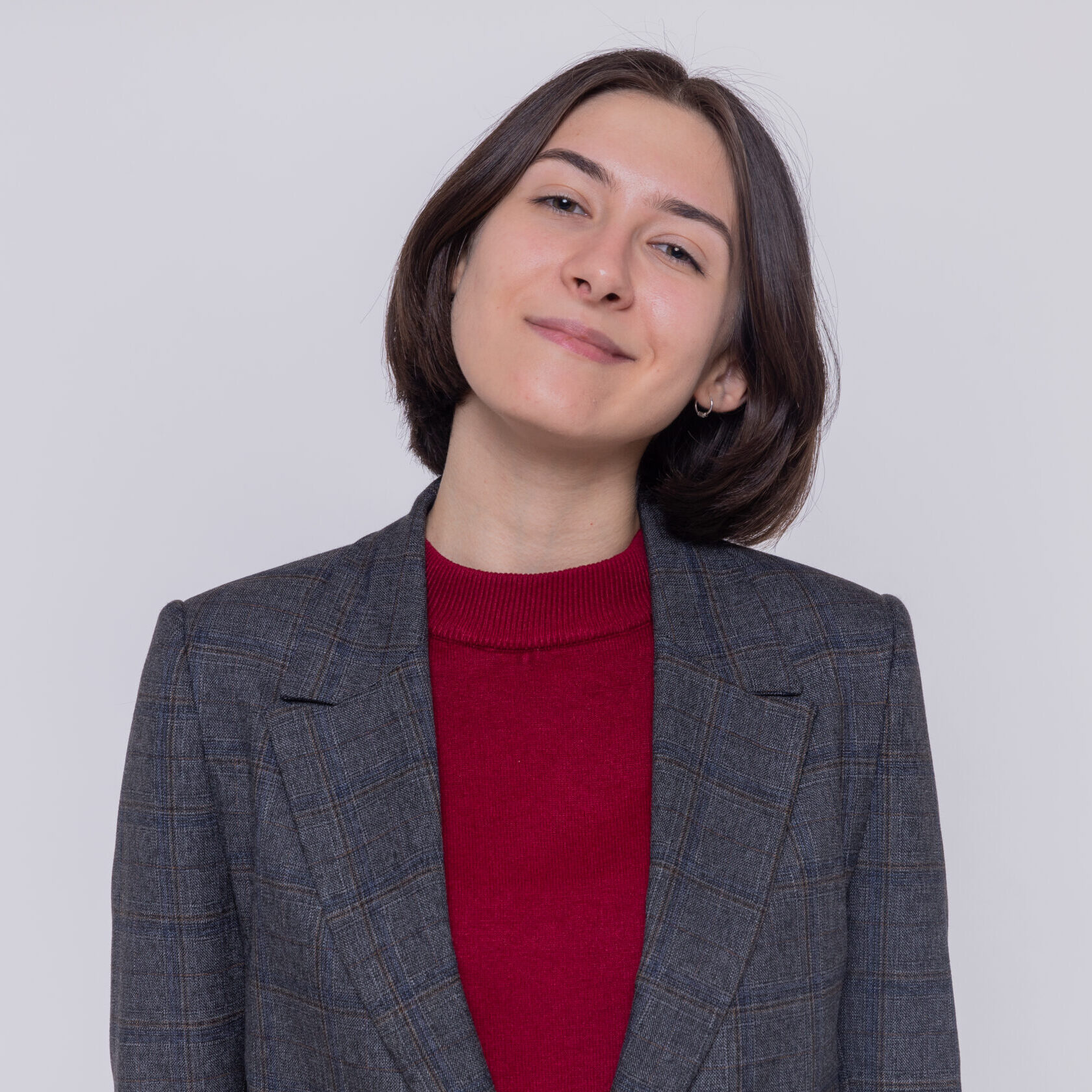 Retrato de uma empresária sorridente com blazer de xadrez, olhando para a câmara com confiança, representando a satisfação do cliente com os serviços de contabilidade e fiscalidade da Mundiempresarial.